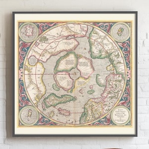 May include: Framed vintage map print showing a detailed, circular world map with intricate illustrations and text. The map is mainly beige, with green, red, and blue accents. The frame is dark, and the print is displayed against a white brick wall.