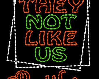 May include: A black and white image of a sign with the text "THEY NOT LIKE US" in green and orange letters. The word "Rattlers" is written in orange letters below the sign.
