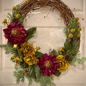 May include: A grapevine wreath decorated with burgundy and yellow flowers, pine cones, and green foliage.