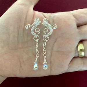 May include: A pair of silver wire earrings with teardrop-shaped iridescent crystals hanging from the bottom.