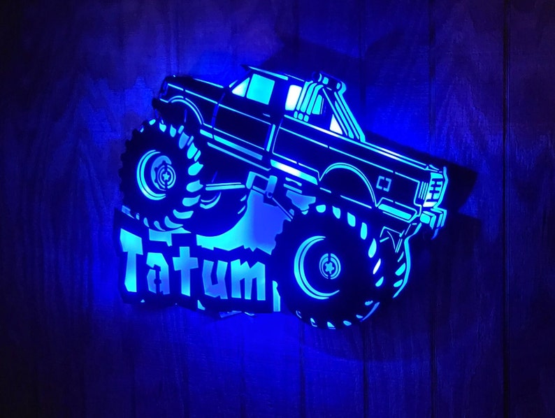 May include: A blue illuminated wooden cutout of a monster truck with the name Tatum in a stylized font.