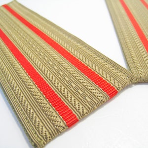 May include: Two beige fabric shoulder boards with two red stripes each. The shoulder boards are sewn together at the top.