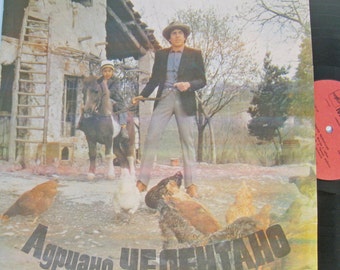 May include: A vintage vinyl record cover featuring a man in a suit and hat standing with a horse and a child. The cover has a rustic background with a wooden building and a ladder. The text "Adriano Celentano" is printed in large, bold letters at the bottom of the cover.