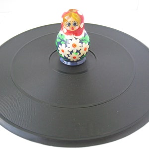 Peut inclure: Un disque vinyle noir avec une petite poupée en bois avec un motif floral rouge, blanc et bleu sur le dessus.