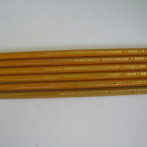 Pode incluir: Seis lápis amarelos com letras douradas, com as inscrições "HARDTMUTH KOH-I-NOOR" e "1500" com diferentes graduações. Os lápis estão dispostos horizontalmente sobre um fundo branco. O texto inclui a palavra "CZECHOSLOVAKIA".