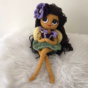 May include: Crocheted doll with brown hair, a purple flower crown, and a green dress holding a bouquet of purple flowers.