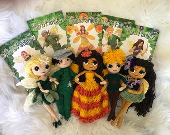 May include: Six crocheted dolls, each with a different color scheme and design. The dolls are dressed in green, orange, yellow, and brown. The dolls are surrounded by several books with the title "Herb Fairies" on the cover.