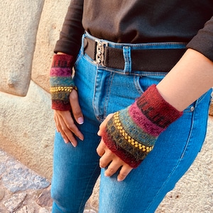 May include: A pair of colorful knitted wrist warmers with gold beads. The wrist warmers are red, pink, blue, green, and brown. The wrist warmers are worn on a person's wrists.