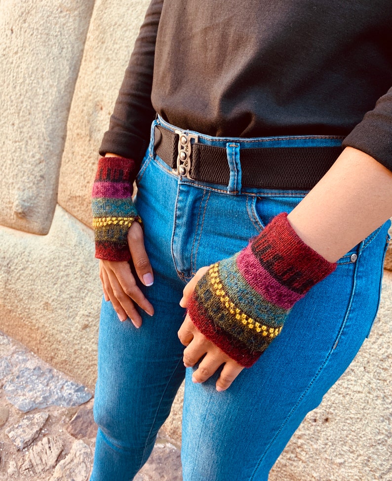 May include: A pair of colorful knitted wrist warmers with gold beads. The wrist warmers are red, pink, blue, green, and brown. The wrist warmers are worn on a person's wrists.