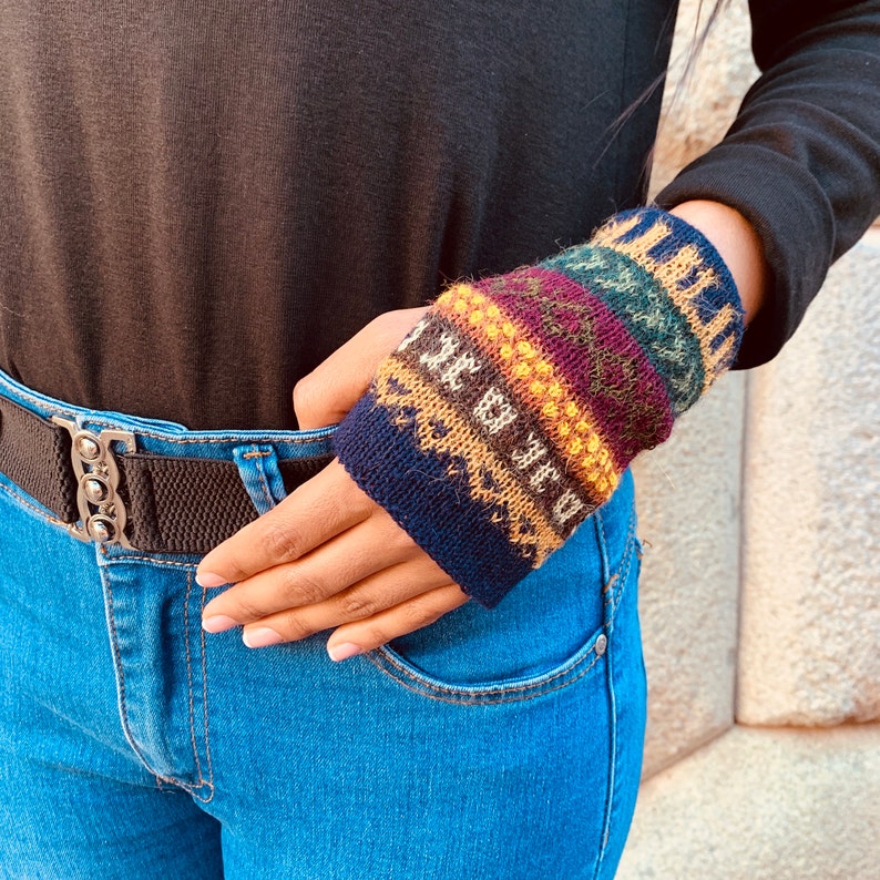 May include: A close-up of a person's hand wearing a colorful knitted wrist warmer with a blue, brown, yellow, red, and green pattern.