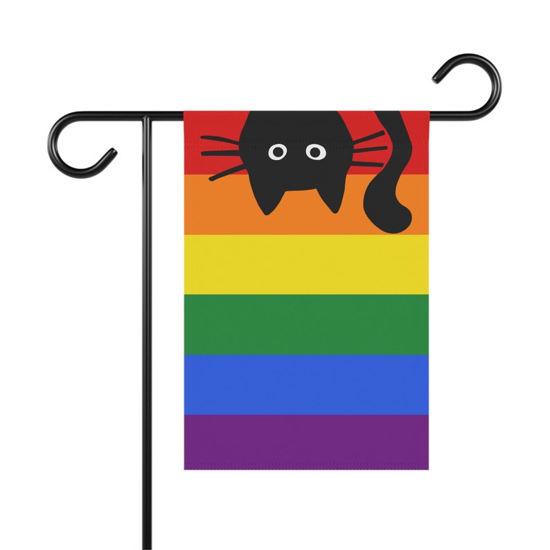 May include: A rainbow pride flag with a black silhouette of a cat looking over the top. The flag is attached to a black metal garden flag stand.