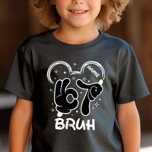 Puede incluir: Camiseta negra con un dise&ntilde;o gr&aacute;fico blanco que presenta manos al estilo de Mickey Mouse formando el n&uacute;mero 67. La palabra "BRUH" est&aacute; debajo. Se proporciona un espacio para agregar un nombre.