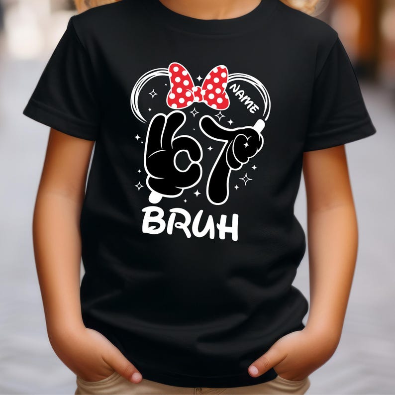 Puede incluir: Camiseta negra con un gr&aacute;fico de dibujos animados. El dise&ntilde;o incluye un lazo de lunares rojos y blancos, el n&uacute;mero 67 en un estilo dibujado a mano y la palabra "BRUH" en letras blancas. Se puede agregar un nombre al dise&ntilde;o.