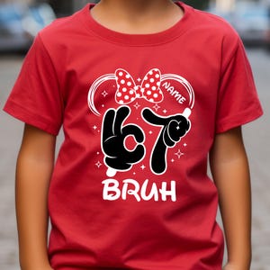 Puede incluir: Camiseta roja con un gr&aacute;fico blanco. El dise&ntilde;o incluye un lazo de lunares, el n&uacute;mero 67 en negro y la palabra "BRUH" en blanco. Hay espacio para un nombre.