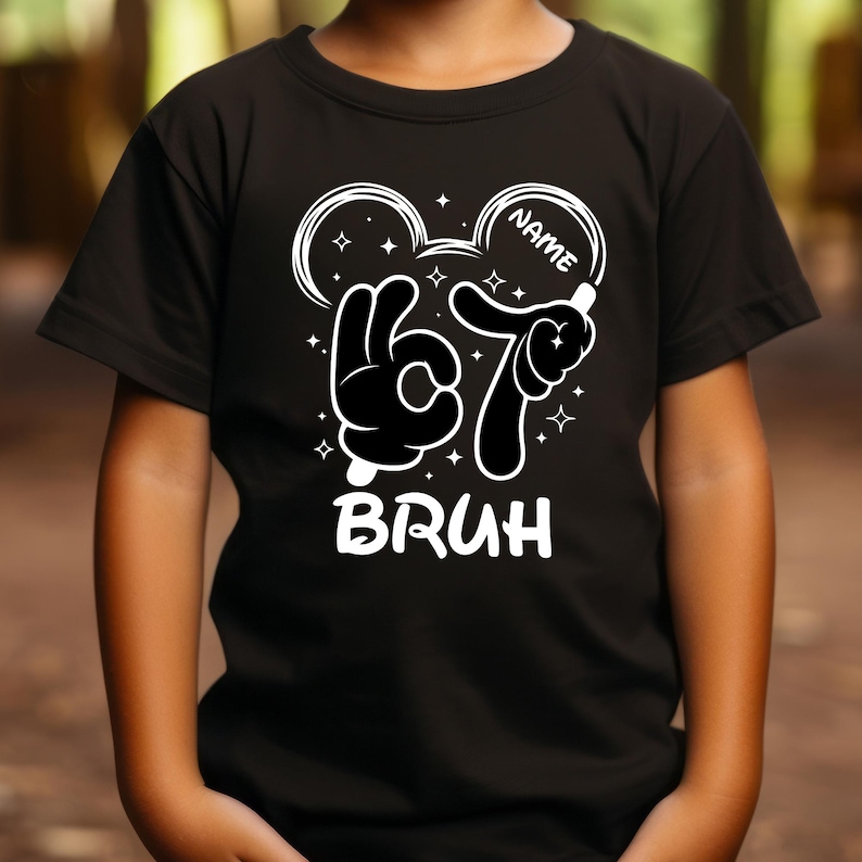 Puede incluir: Camiseta negra con un gr&aacute;fico blanco que muestra manos de dibujos animados formando el n&uacute;mero 67, con la palabra "BRUH" debajo. El dise&ntilde;o incluye un contorno de cabeza estilo Mickey Mouse y espacio para un nombre, adem&aacute;s de estrellas.
