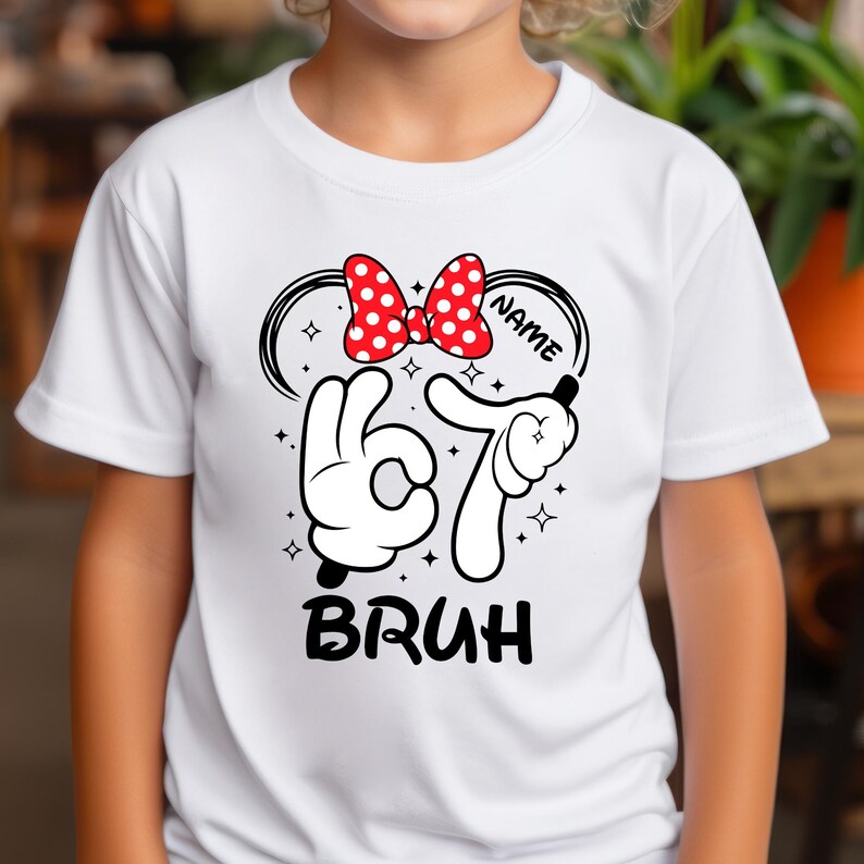 Puede incluir: Camiseta blanca con un dise&ntilde;o de dibujos animados. Presenta un lazo rojo de lunares, el n&uacute;mero 67 y la palabra "BRUH" en negro. El dise&ntilde;o incluye manos de dibujos animados y estrellas, con espacio para un nombre.