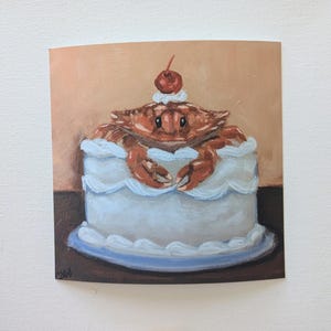 May include: A blue and white frosted cake with a red cherry on top. A brown crab is sitting on top of the cake, with its claws resting on the frosting.