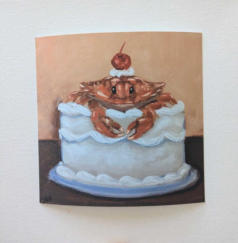 May include: A blue and white frosted cake with a red cherry on top. A brown crab is sitting on top of the cake, with its claws resting on the frosting.