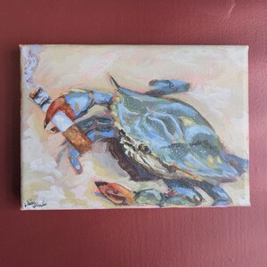 May include: An original painting on canvas depicts a blue crab smoking a cigarette. The crab is painted in shades of blue, with orange and red accents. The background is a light beige, and the painting is signed in the lower left corner.