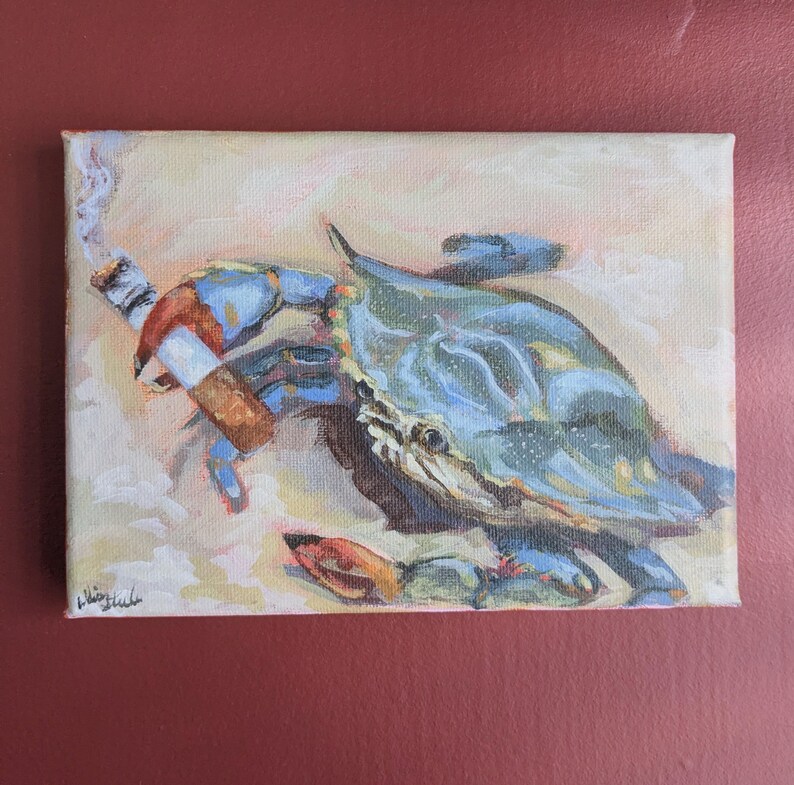 May include: An original painting on canvas depicts a blue crab smoking a cigarette. The crab is painted in shades of blue, with orange and red accents. The background is a light beige, and the painting is signed in the lower left corner.