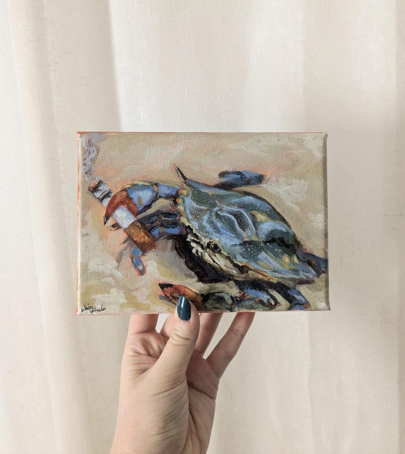May include: An original oil painting of a blue crab smoking a cigar. The crab is painted in shades of blue and brown, with a detailed depiction of the crab's shell and claws. The background is a soft, neutral color, with the artist's signature in the lower left corner.