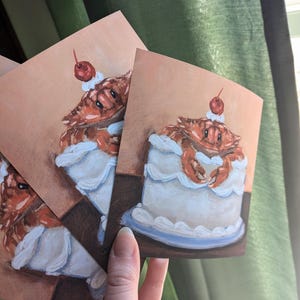May include: Three illustrated cards featuring a crab wearing a cherry on top of a white cake with blue frosting.