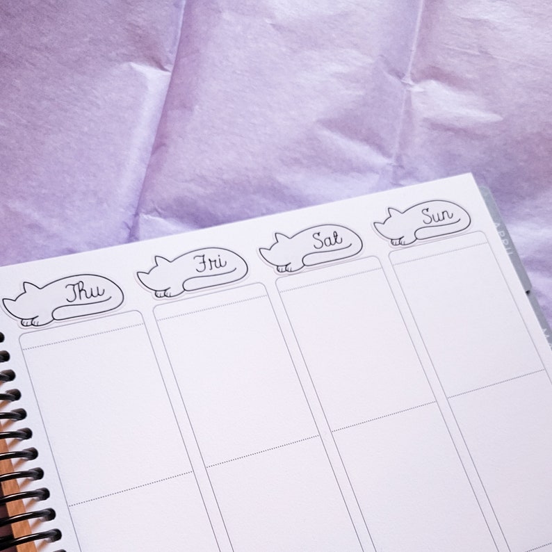 May include: A white planner with black cat stickers for each day of the week. The stickers say "Thu", "Fri", "Sat", and "Sun".