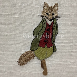 Könnte beinhalten: Gestickte Abbildung eines Fuchses, der eine grüne Jacke, eine rote Weste und eine braune Hose trägt. Der Fuchs hat einen braunen Schwanz und steht auf einem Bein.