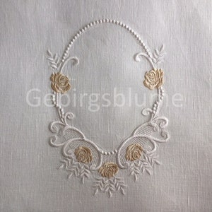 Op de afbeelding: Wit linnen stof met een geborduurde ovale lijst met een parelrand en vijf gouden rozen.