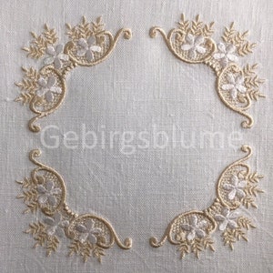 May include: A white linen fabric with a decorative embroidered border in gold and white. The border features a repeating pattern of stylised flowers and leaves.