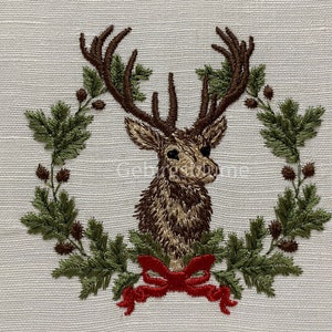 May include: Embroidered design of a deer head with antlers surrounded by a wreath of green leaves and brown berries. A red bow is tied at the bottom of the wreath.