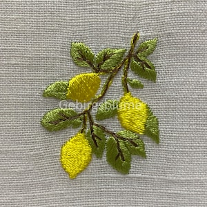 以下が含まれることがあります： 白いリネン地に、刺繍されたレモンの枝。レモンは黄色で、葉は緑色です。