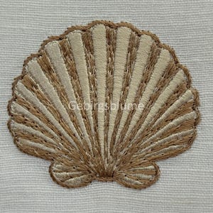 Puede incluir: Parche bordado de concha marina en tonos beige y marrón, con el texto "Gebirgsblume" visible. El parche está cosido sobre un fondo de tela blanca. El diseño de la concha presenta costuras detalladas.