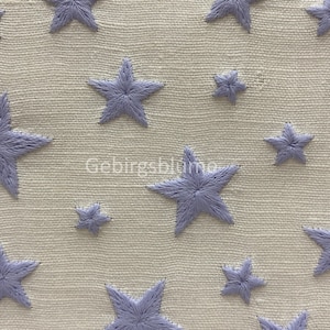 以下が含まれることがあります： 微妙な質感の白い生地に、さまざまなサイズのラベンダー色の刺繍された星が繰り返しパターンで施されています。