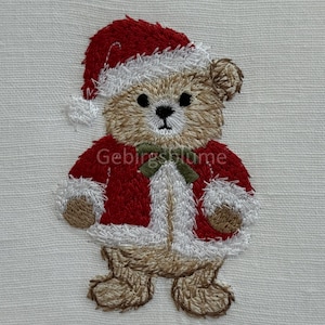 Könnte beinhalten: Gestickter Teddybär mit Weihnachtsmütze und Mantel. Der Bär ist hellbraun mit rotem Mantel und Hut, die mit Weiß verziert sind. Eine grüne Schleife befindet sich am Hals. Der Text "Gebirgsblume" steht auf dem Mantel.