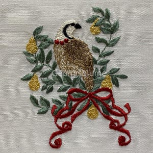 May include: Embroidered design of a brown bird with red ribbon and green leaves on a white linen background.