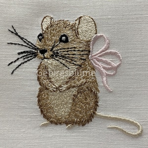 May include: Embroidered brown mouse with a pink bow. The mouse is standing on its hind legs with its paws together. It has a long tail and whiskers.