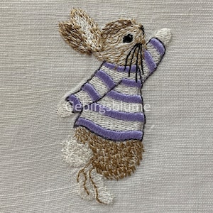 Könnte beinhalten: Gestickter Hasen-Patch mit einem lila-weiß gestreiften Shirt. Der Hase steht auf seinen Hinterbeinen mit erhobenen Vorderpfoten.