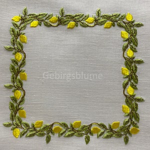 以下が含まれることがあります： レモンの刺繍が施された白いリネン製のテーブルクロス。レモンは黄色で、葉は緑色です。
