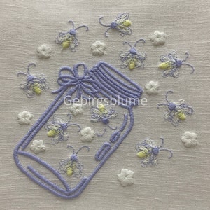 Puede incluir: Un tarro de vidrio morado con un lazo blanco y un diseño floral. El tarro está lleno de luciérnagas amarillas. El fondo es una tela de lino blanca con un diseño floral.