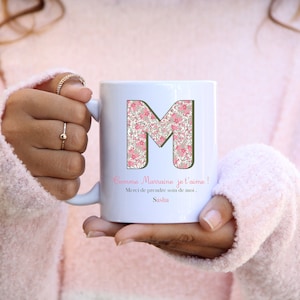 Peut inclure: Mug en céramique blanche avec une lettre M florale rose et le texte "Comme Marraine je t'aime! Merci de prendre soin de moi, Sasha".