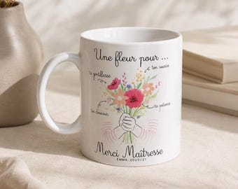 Puede incluir: Taza de cerámica blanca con asa, decorada con una ilustración de ramo de flores. El texto incluye "Une fleur pour..." y "Merci Maîtresse" con un nombre y una fecha. Un regalo atento.