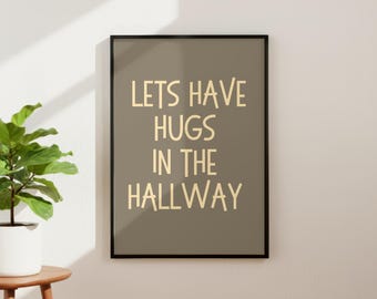 May include: A framed wall art print featuring a muted olive green background with the text "LETS HAVE HUGS IN THE HALLWAY" printed in a light cream, sans-serif font. The rectangular frame is black and thin, surrounding the centered text design.