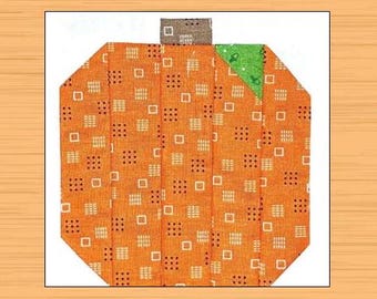 Puede incluir: Una calabaza de patchwork con un tallo marrón y una hoja verde. La calabaza está hecha de tela naranja con un patrón geométrico blanco y negro.