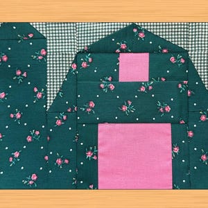 Può includere: Un blocco di trapunta con un motivo floreale verde e bianco e un centro rosa. Il blocco è composto da diversi quadrati e rettangoli più piccoli.