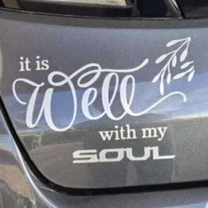 May include: White decal with the words "it is Well with my SOUL" in a script font, with a sprig of leaves. The decal is affixed to a gray vehicle surface.