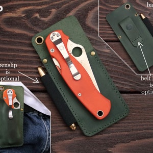 Pu&ograve; includere: Portacoltelli e penne in pelle verde con passante per cintura opzionale. Il portacoltelli ha uno slot per un coltello e una penna. Il coltello &egrave; arancione e ha una lama argentata. La penna &egrave; nera. Il portacoltelli &egrave; su una superficie di legno.