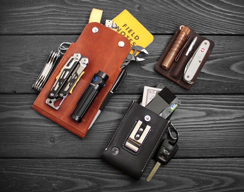 May include: Three leather pouches with various tools and accessories. The pouches are brown and black and have different compartments for carrying items. The pouches are on a black wooden surface.
