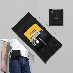 Könnte beinhalten: Schwarze Nylon-Gürteltasche mit Reißverschlussfach und zwei elastischen Schlaufen. Die Tasche ist gefüllt mit einem Multitool, einem Stift, Kreditkarten und einem gelben Kartenhalter mit dem Aufdruck "FIELD".