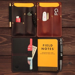 Puede incluir: Dos cubiertas de cuaderno de cuero marr&oacute;n con bolsillos y una cubierta de cuaderno de cuero negro con bolsillos. La cubierta negra tiene un cuaderno amarillo con el texto "FIELD NOTES" y "48-Page Memo Book / Ledger Durable Materials / Made in the U.S.A."